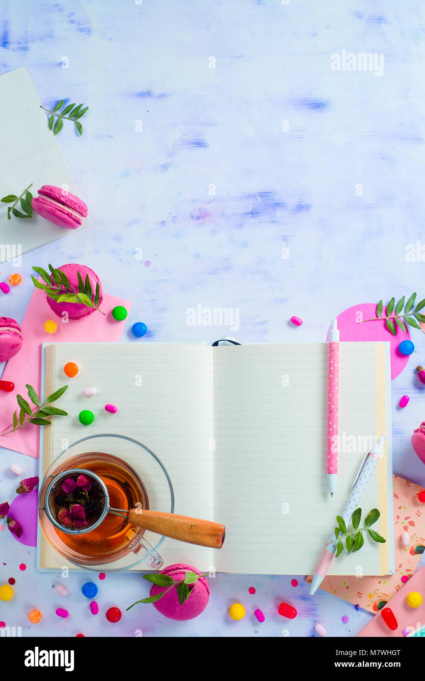 Weibliche Schriftsteller Arbeitsplatz mit einem offenen Notepad oder Tagebuch. Bunten süßen Snacks, Hard Candy, und Rosa macarons auf einem hellen Hintergrund mit Kopieren s Stockfoto