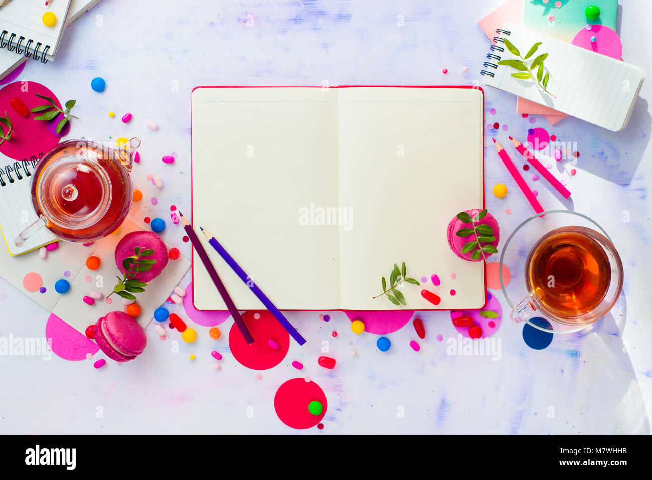 Weibliche Schriftsteller Arbeitsplatz mit einem offenen Notepad oder Tagebuch. Bunten süßen Snacks, Hard Candy, und Rosa macarons auf einem hellen Hintergrund mit Kopieren s Stockfoto