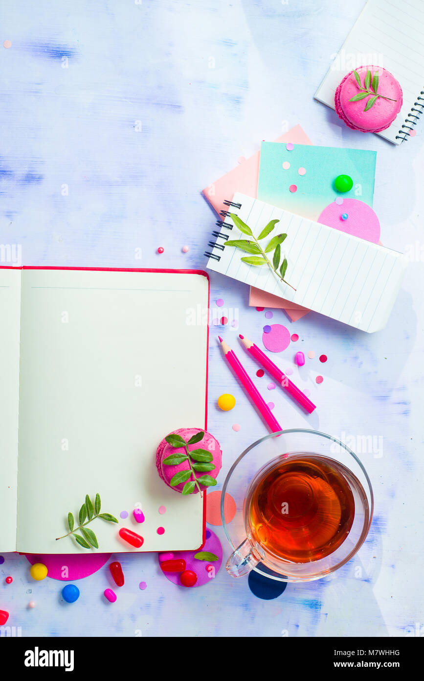 Bunte flach mit einem offenen Buch mit leeren Seiten, Konfetti, Süßigkeiten, Bonbons, rosa Umschlag, Makronen und Tee. Weibliche Schriftsteller Arbeitsplatz mit Stockfoto