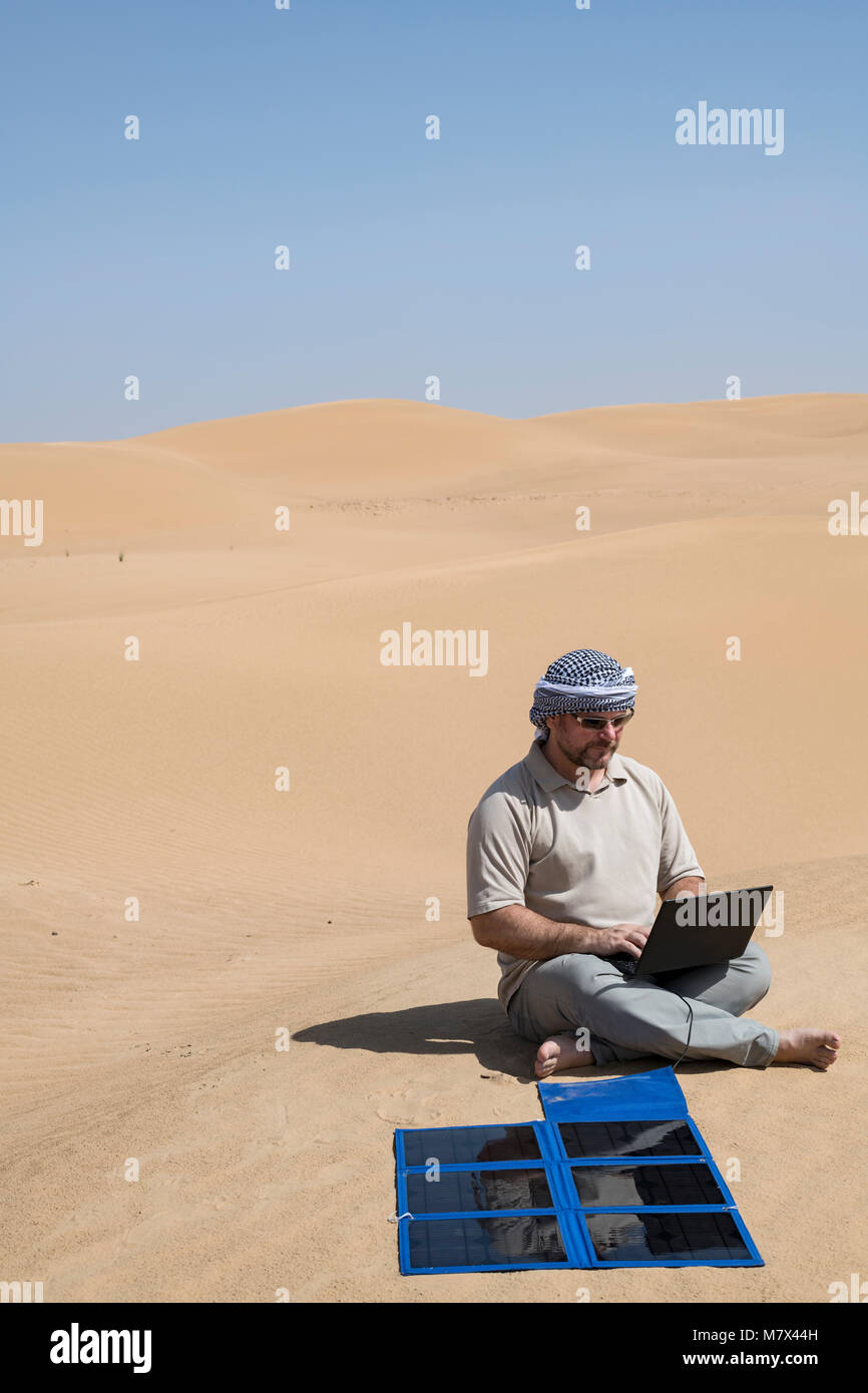 Ein Mann arbeitet ferngesteuert an seinem Laptop neben einem tragbaren Solarmodul in einer Wüste, Selbstvertrauen und Nachhaltigkeit in einer ferngesteuerten Umgebung mit Kopierraum Stockfoto