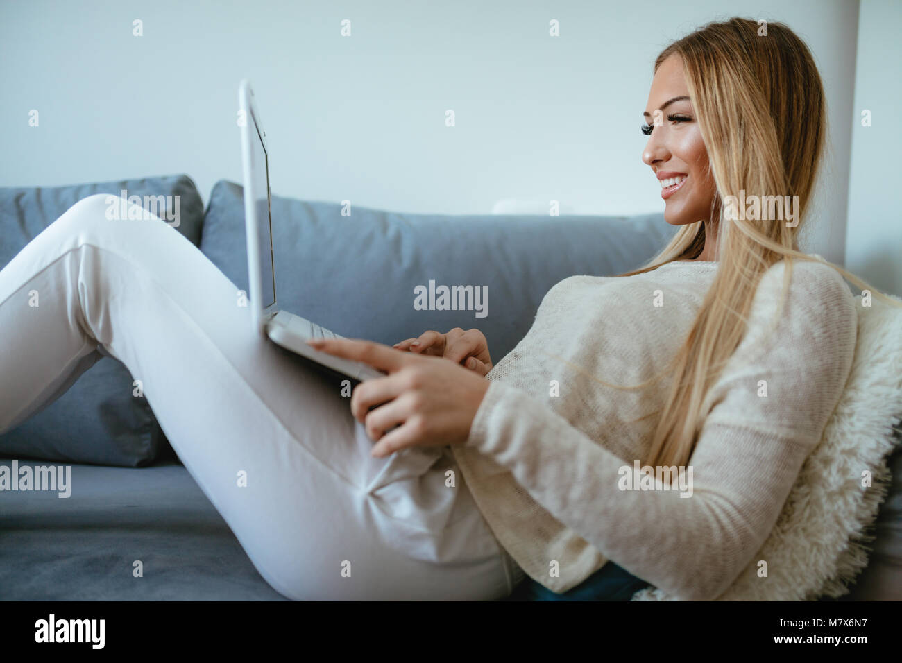Attraktive lächelnde Mädchen sitzt auf einem Bett und mit Laptop. Sie surfen im Internet und Social Media. Stockfoto