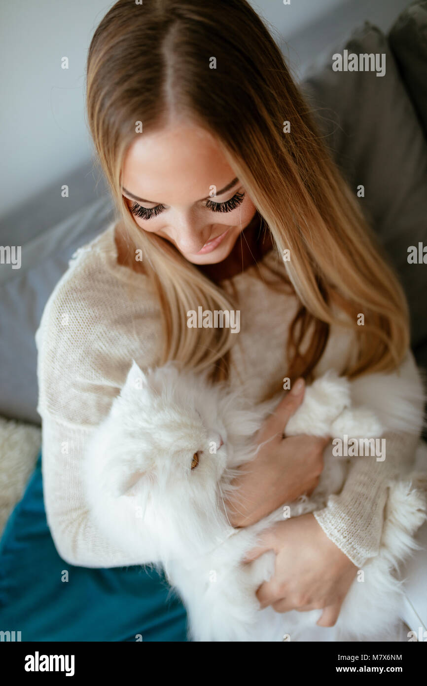 Nette junge Frau zu Hause entspannen und umarmt ihre schönen weißen Perser Katze. Stockfoto