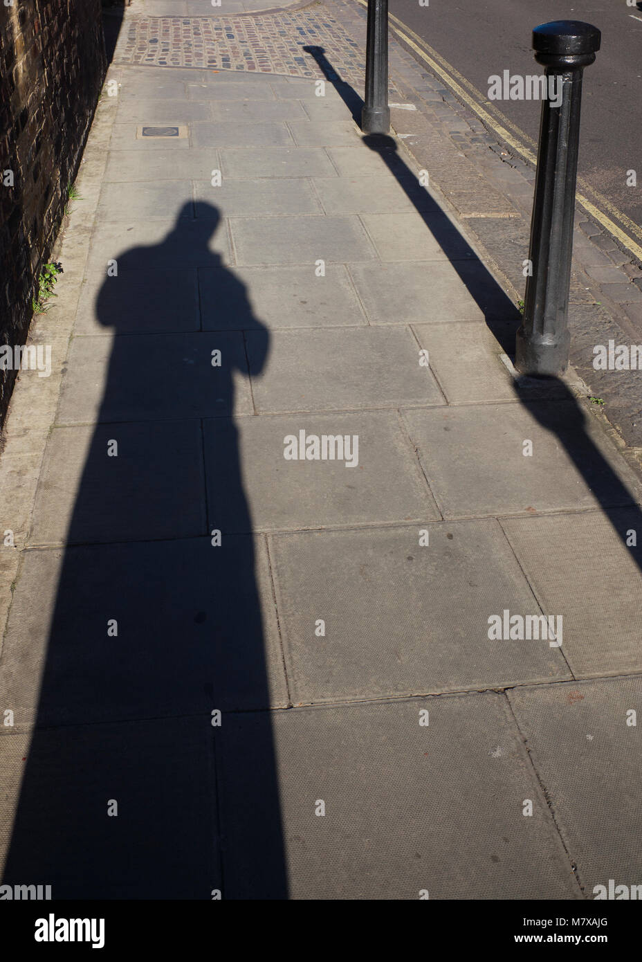 Langer Schatten der Figur auf der Straße in hellem Sonnenlicht Stockfoto