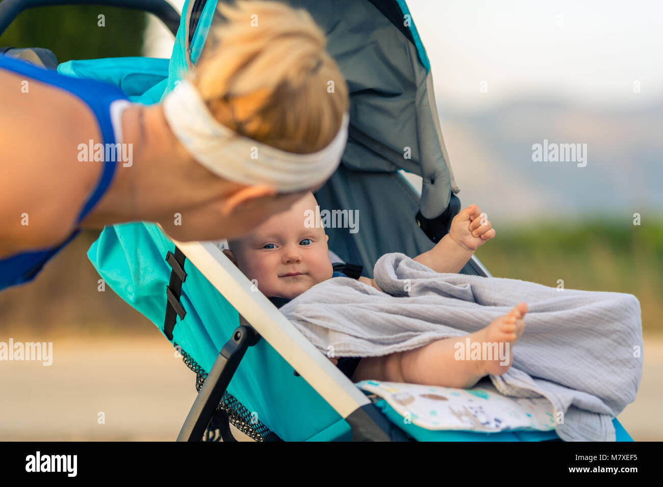 Mutter mit Kind im Kinderwagen bei Mutterschaft bei Sonnenuntergang und Bergwelt. Joggen oder Walken Frau mit Kinderwagen bei Sonnenuntergang. Beautifu Stockfoto