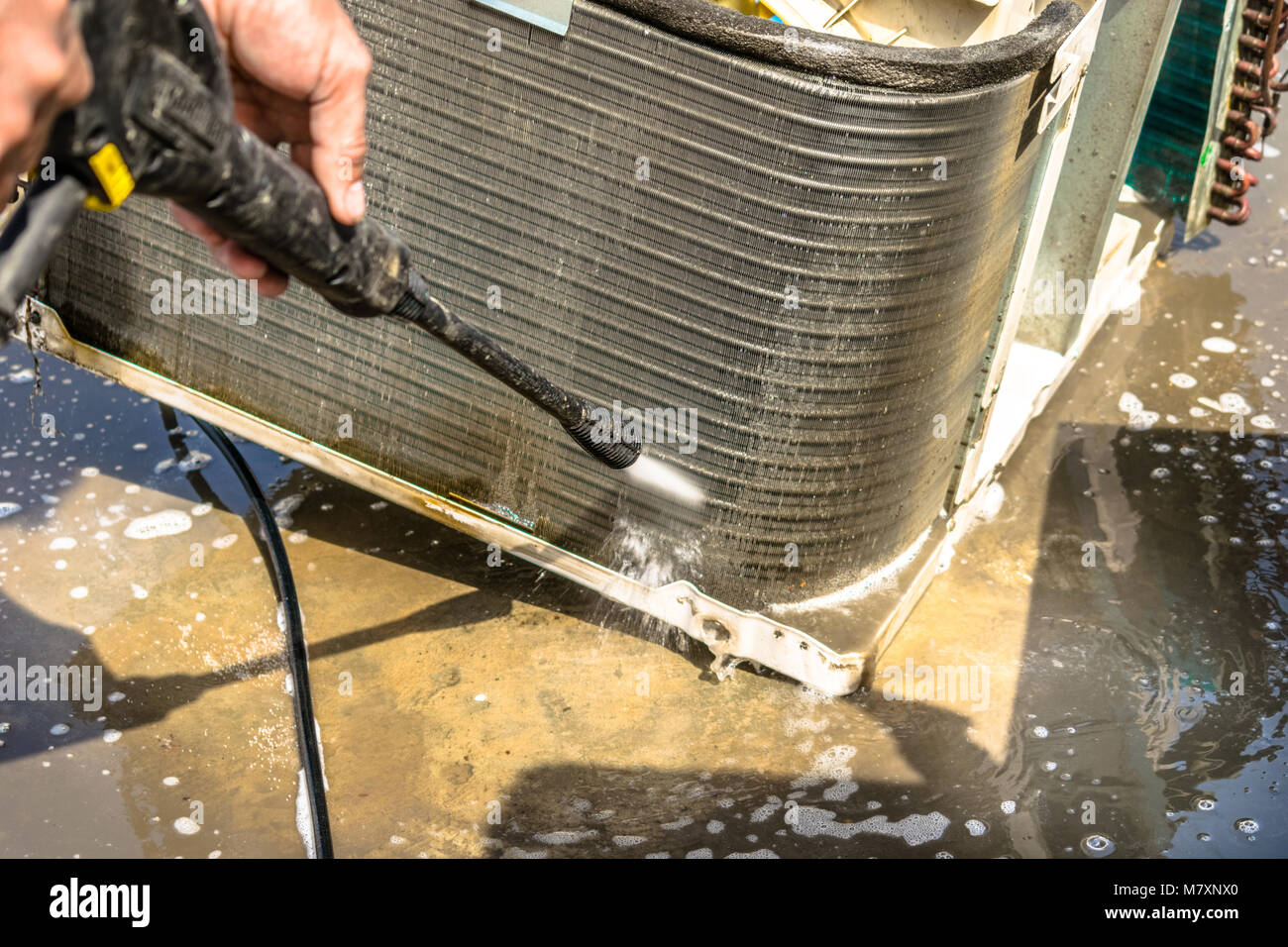 Einen professionellen Elektriker ist die Reinigung der Fenster Klimaanlage auf dem Dach eines Hauses mit seinem hohen Druck Wasser Pistole Stockfoto