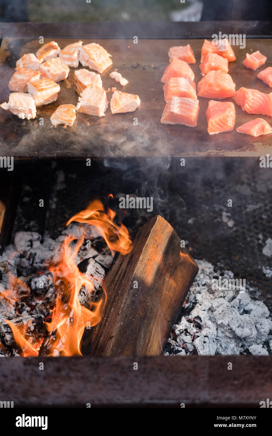 Lecker lachs Stücke auf einem Grill mit Flammen, die aus dem Holz und Holzkohle Feuer unter Stockfoto