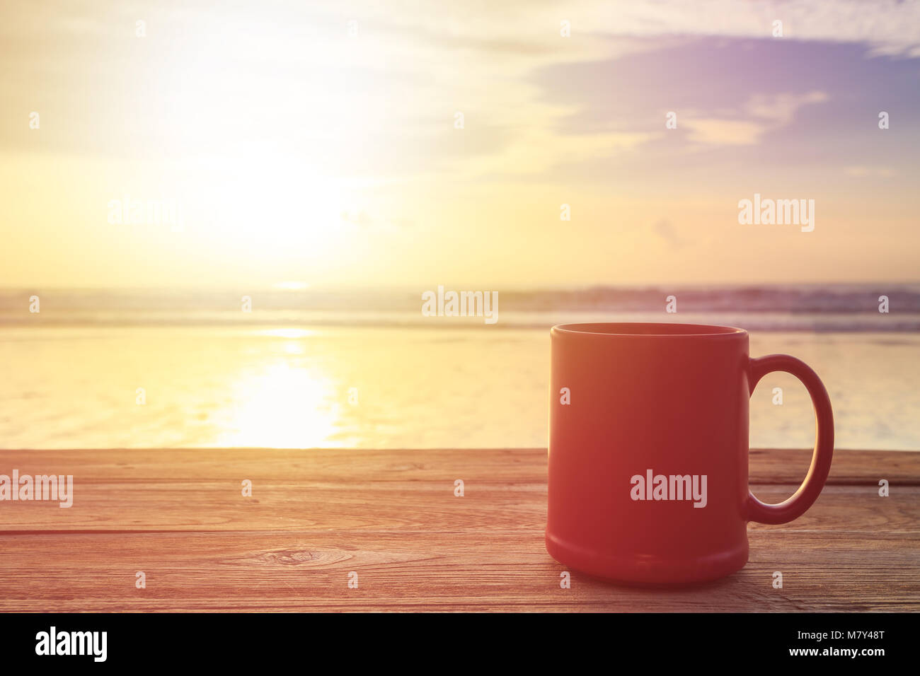 Schließen Sie die rote Kaffeetasse auf Holz Tisch bei Sonnenuntergang oder Sunrise Beach Stockfoto