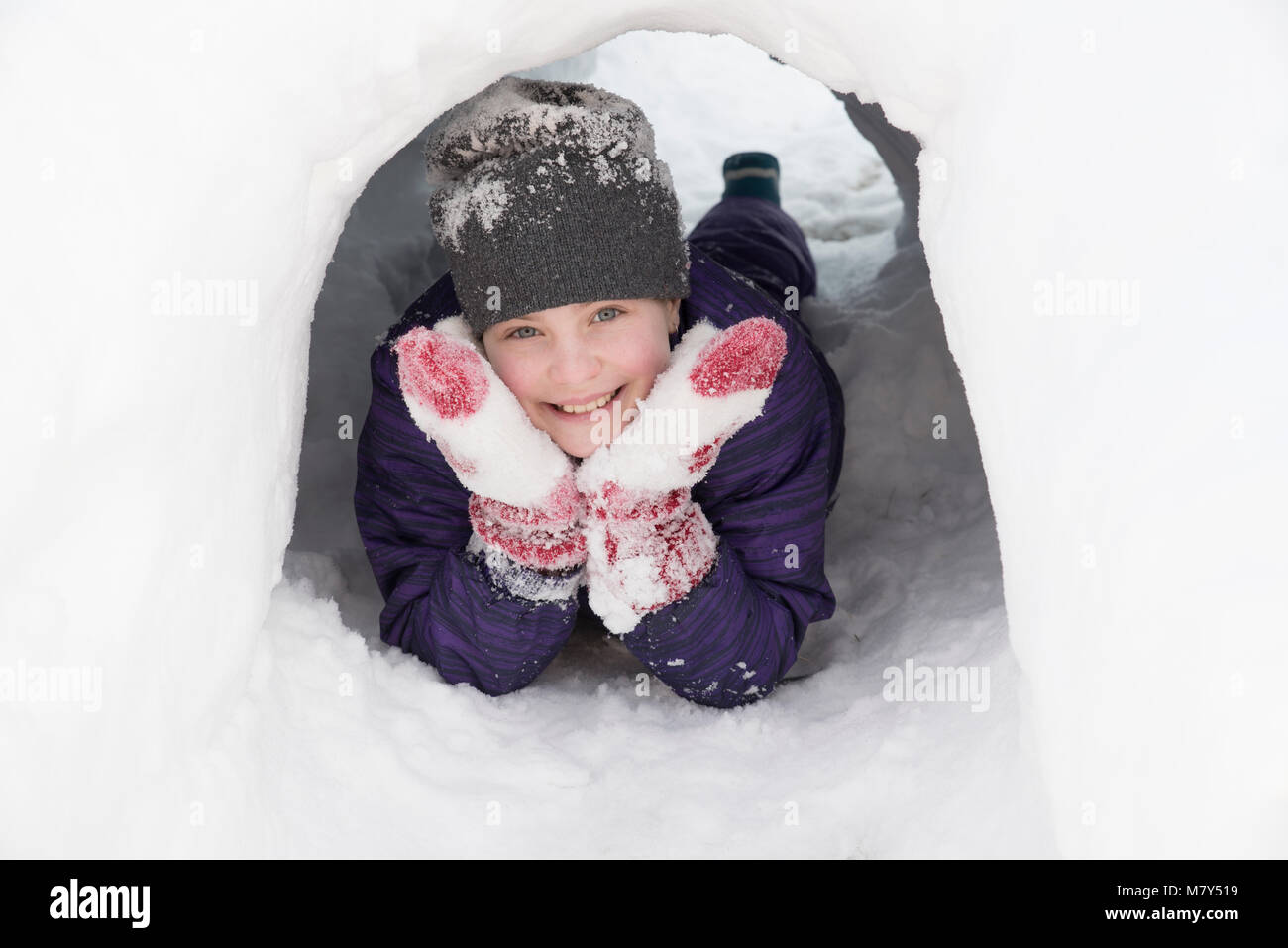 Kanadische Mädchen lächelnd aufliegt und auf Ellbogen mit Kopf auf die Hände am Ausgang eines Snow tunnel Stockfoto