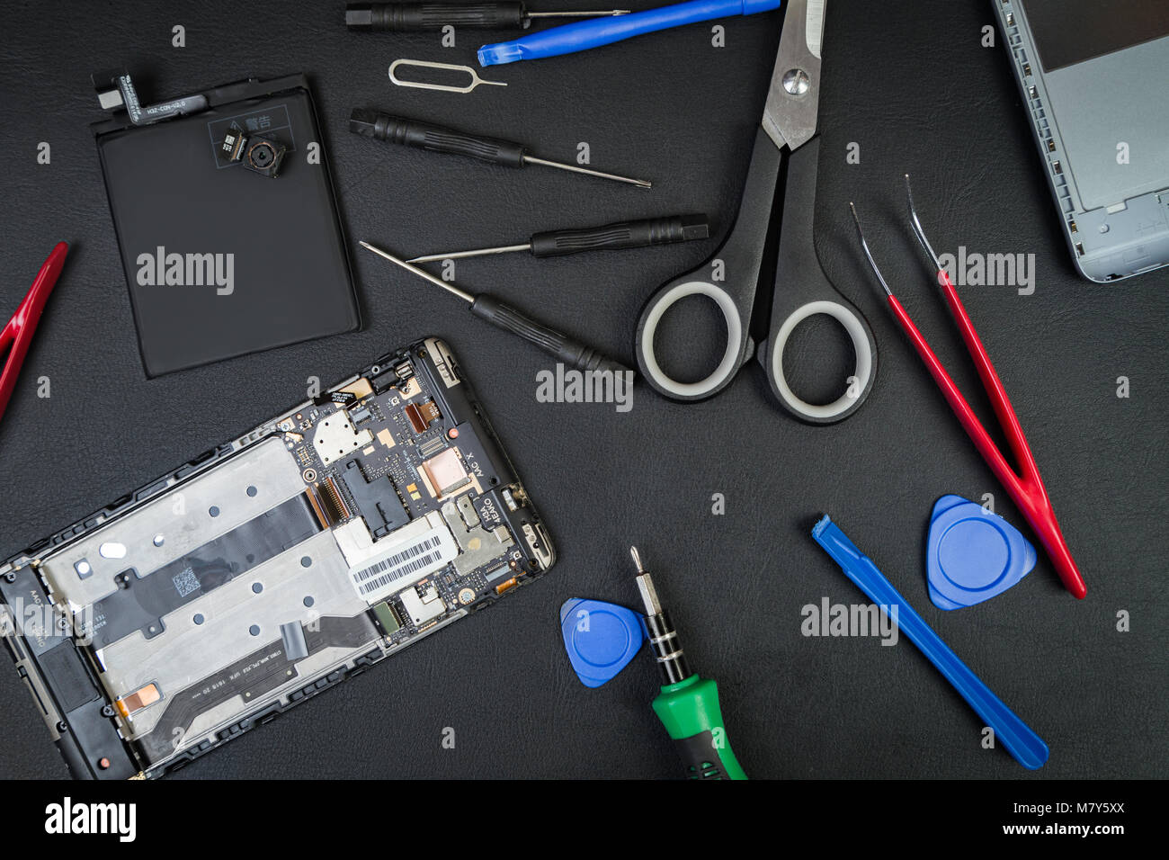 Die Störung auf einem schwarzen Tabelle der Handwerker mit Details der Smartphone- und Spezialwerkzeuge. Die demontierten Telefon in flatlay Stil. Stockfoto