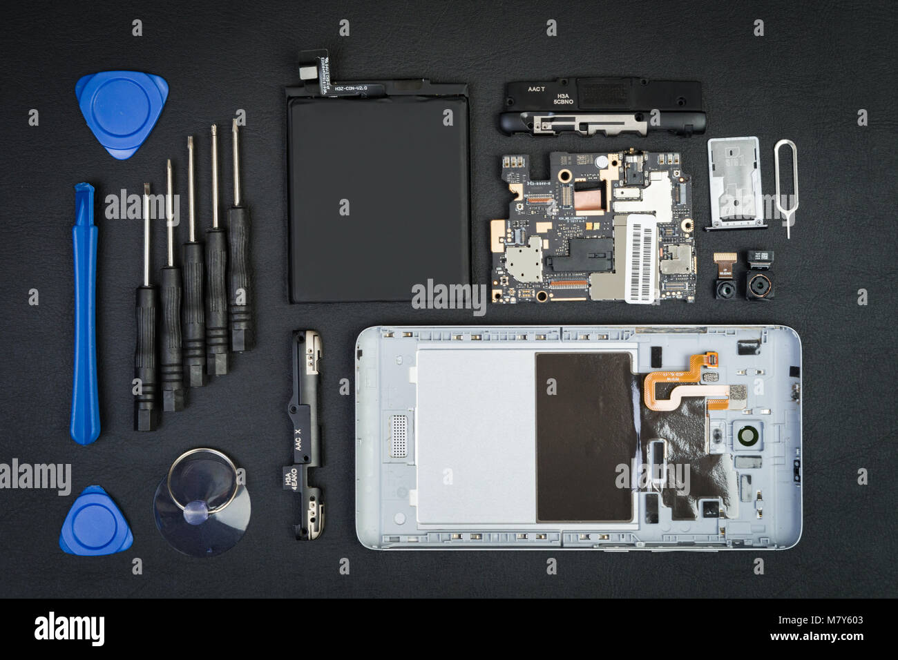 Die demontierten Handy, die mit der entfernten Bildschirm und Sonderwerkzeuge auf dem schwarzen Desktop. Smartphone details in flatlay Stil. Stockfoto