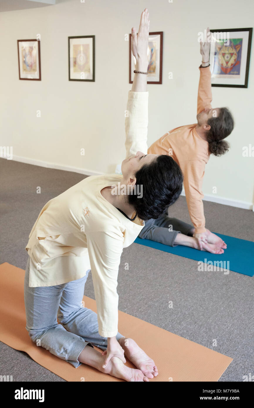 Junge männliche und weibliche Studenten üben ushtrasana - camel Pose in Yoga class. Holding in Pose auf Ihre Yoga Matten auf Teppichboden drinnen in Licht Stockfoto