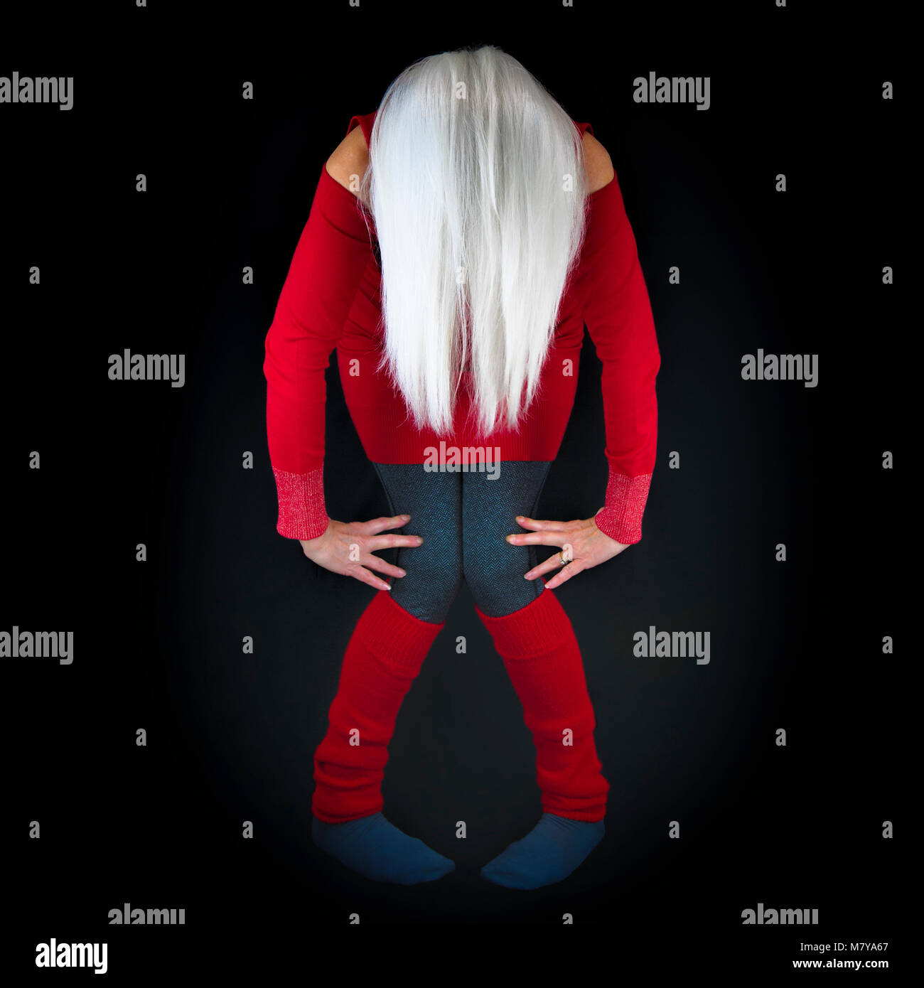 Eine reife Frau, in einer abstrakten künstlerischen Stil posiert, beugte sich in Richtung Kamera mit langen weißen Haaren hängen, das Tragen der roten Pullover und Beinlinge, Stockfoto