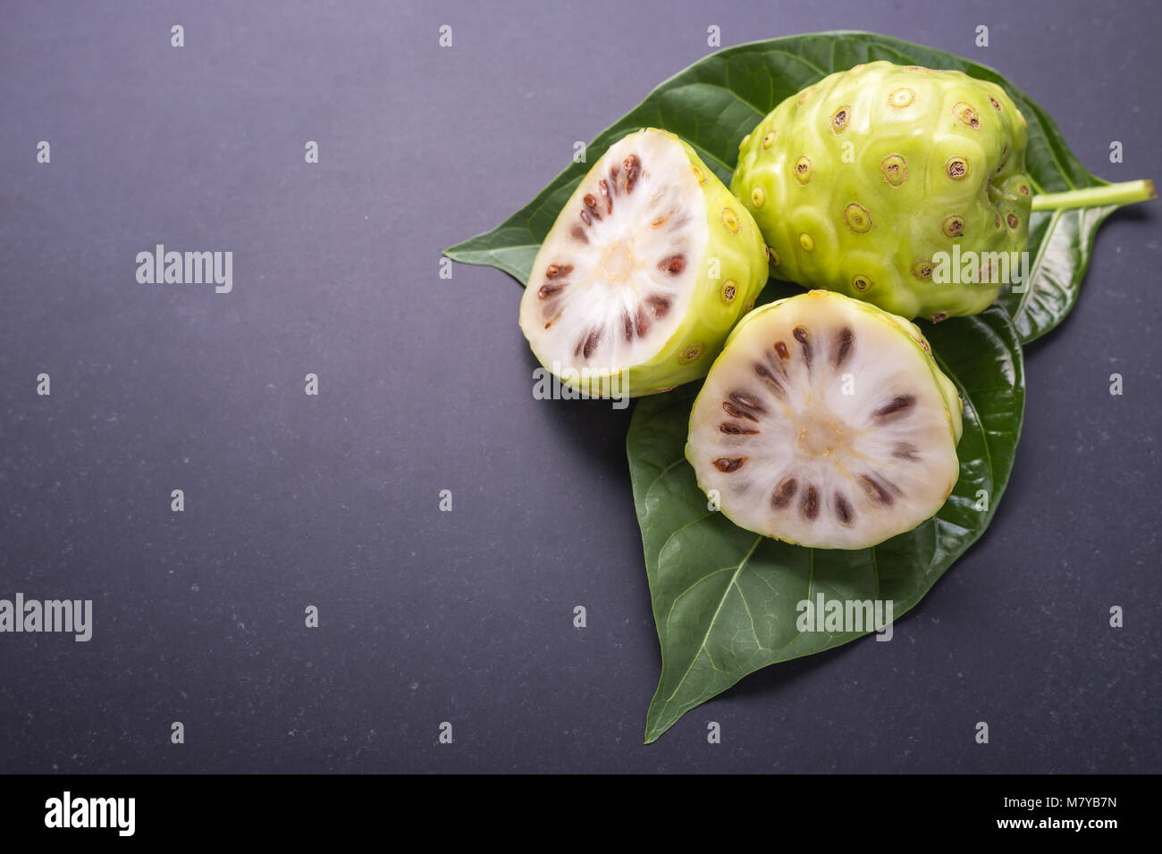 Frucht des Großen morinda (Noni) oder Morinda citrifolia Baum und grüne Blätter auf Schwarz Stein Vorstand Hintergrund Stockfoto