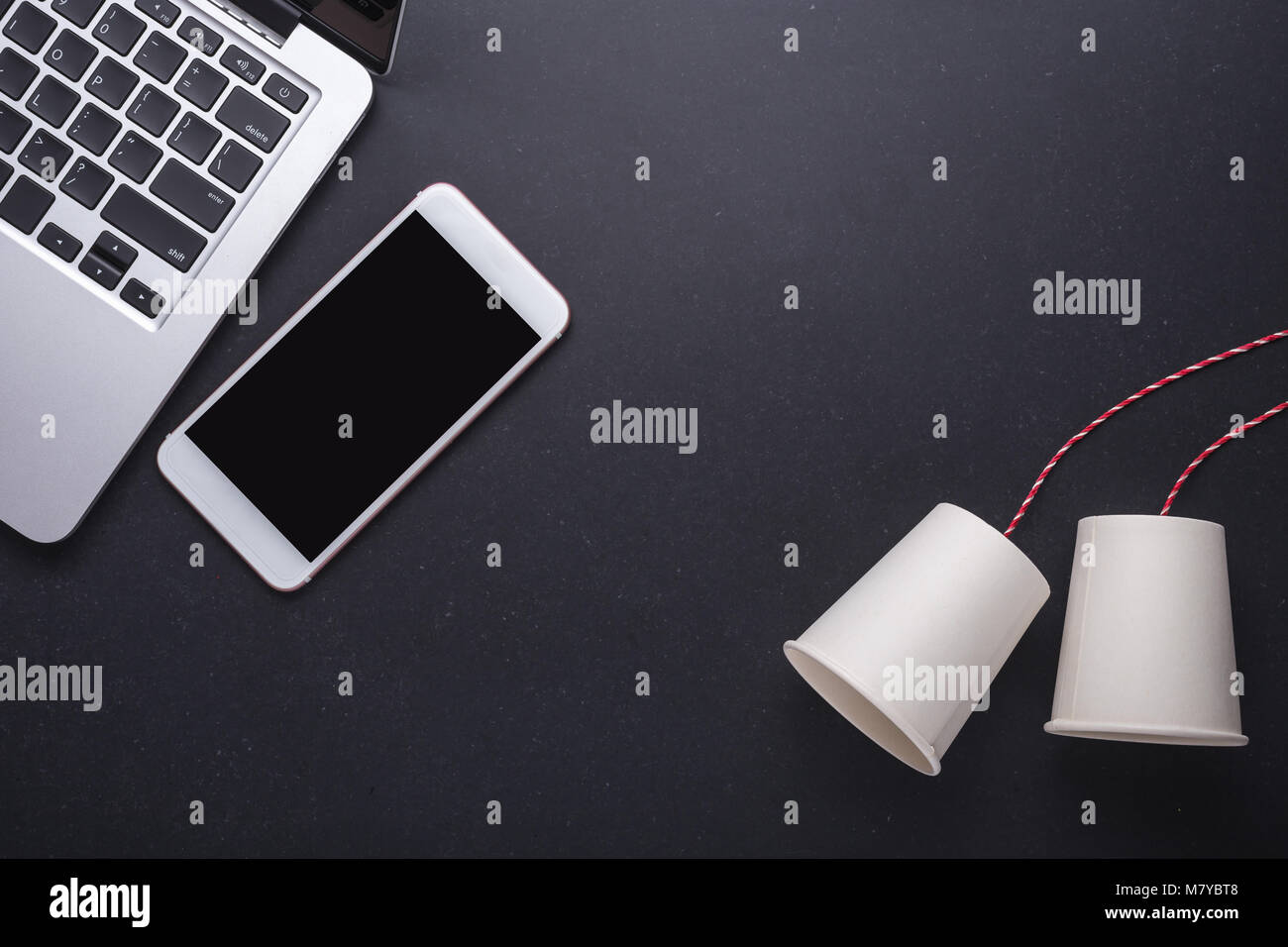 Zwei White Paper Cup verbinden mit dem roten Seil für klassische und moderne Smartphones auf schwarzen Stein Tabelle Vorstand Hintergrund verwendet. Für die Alten vergleichen und Stockfoto