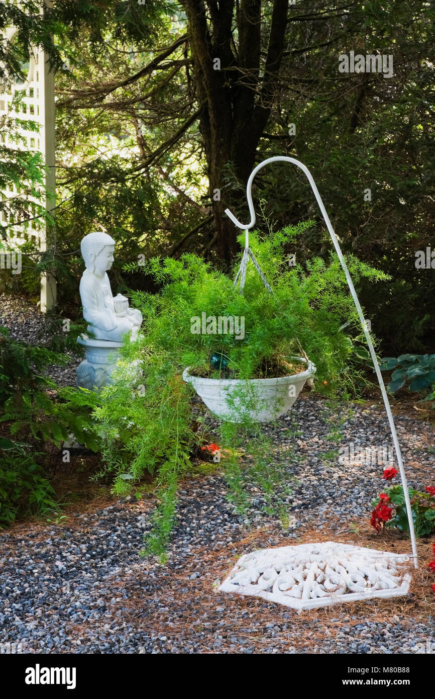 Asparagus officinalis in hängenden Korb auf einem White Metal stehen und ein buddhistischer Mönch Statue in einem gepflegten Wohngebiet Garten im Sommer. Stockfoto
