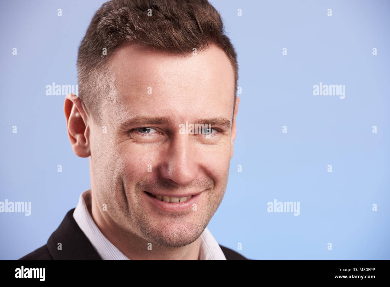 Freundliche Lächeln des jungen Mannes schließen bis auf blauem Hintergrund isoliert Stockfoto