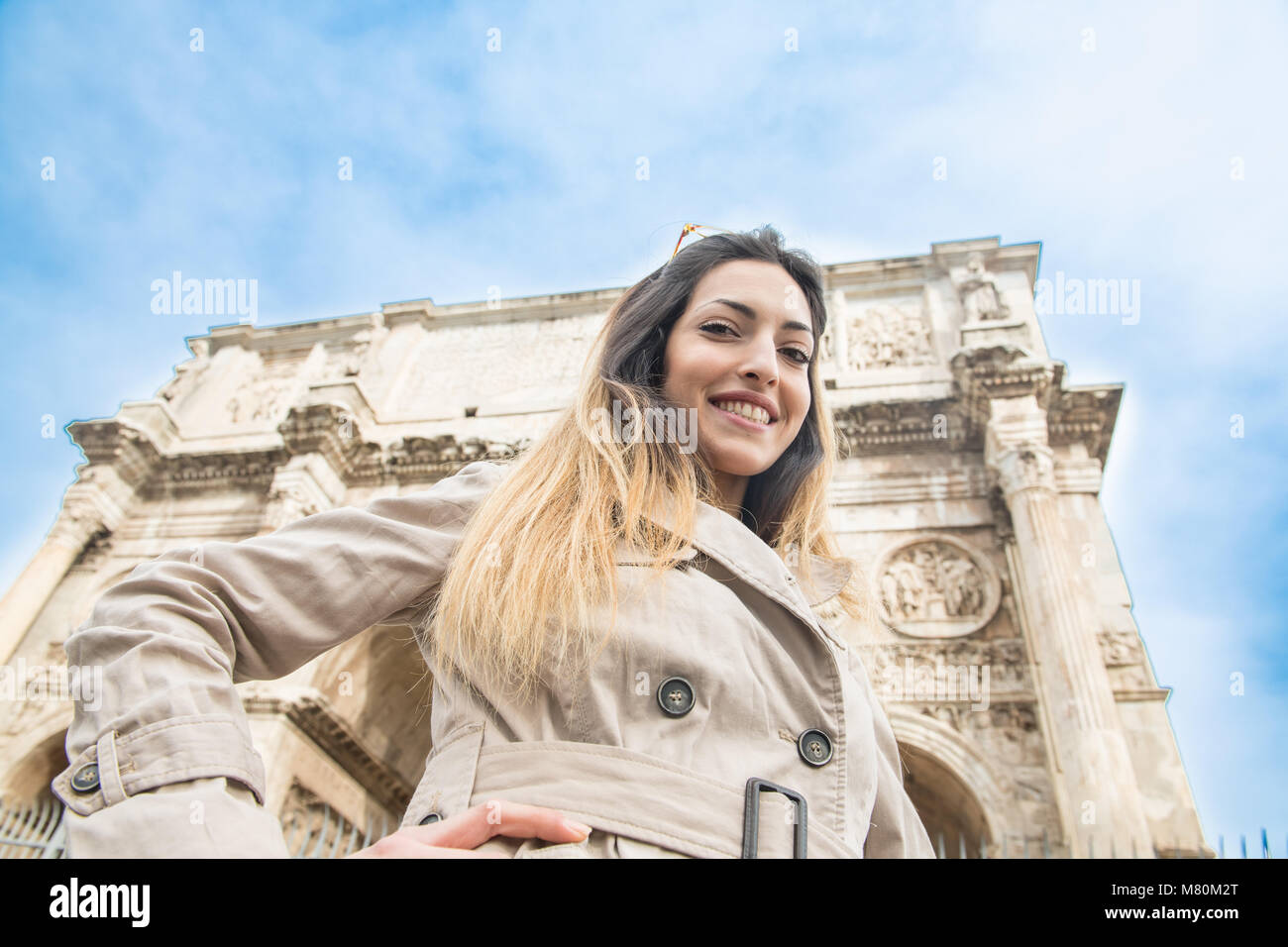 Low Angle View von jungen hübschen Touristische lächelnde Frau mit Kamera, im Hintergrund Triumphbogen des Konstantin Monument in Rom Italien Stockfoto