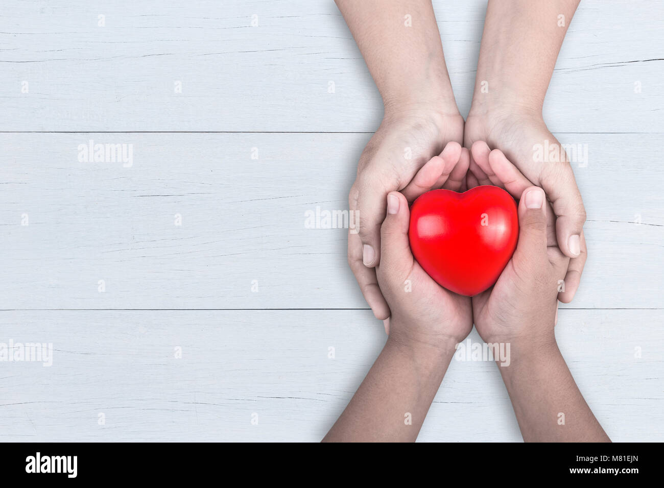 Liebe Mama Konzept: Frau hält ihre jungen Kinder Hände unterstützt Rotes Herz auf braune Holztisch Hintergrund. Freier Platz für Text der Muttertag Feier Stockfoto
