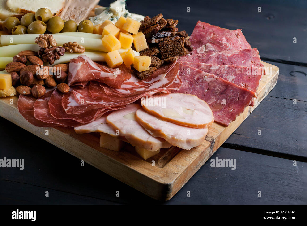 Aus Fleisch und Käse auf einem Schneidebrett sortiert. Geräucherte Wurst, Fleisch aus der Türkei mit Käse, Schinken, Oliven, Nüsse und verschiedene sorten Käse. Low Key. Dunklen Hintergrund Stockfoto