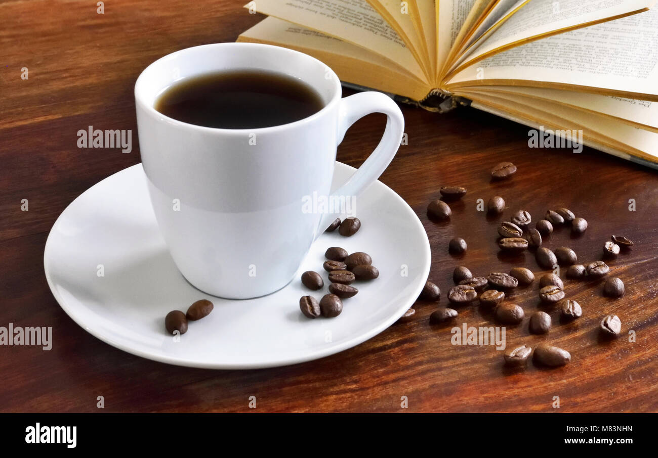 Frühstück Szene mit Kaffeetasse, offenes Buch und Kaffeebohnen auf einem Holztisch. Morgen Szene mit heißem Kaffee. Stockfoto