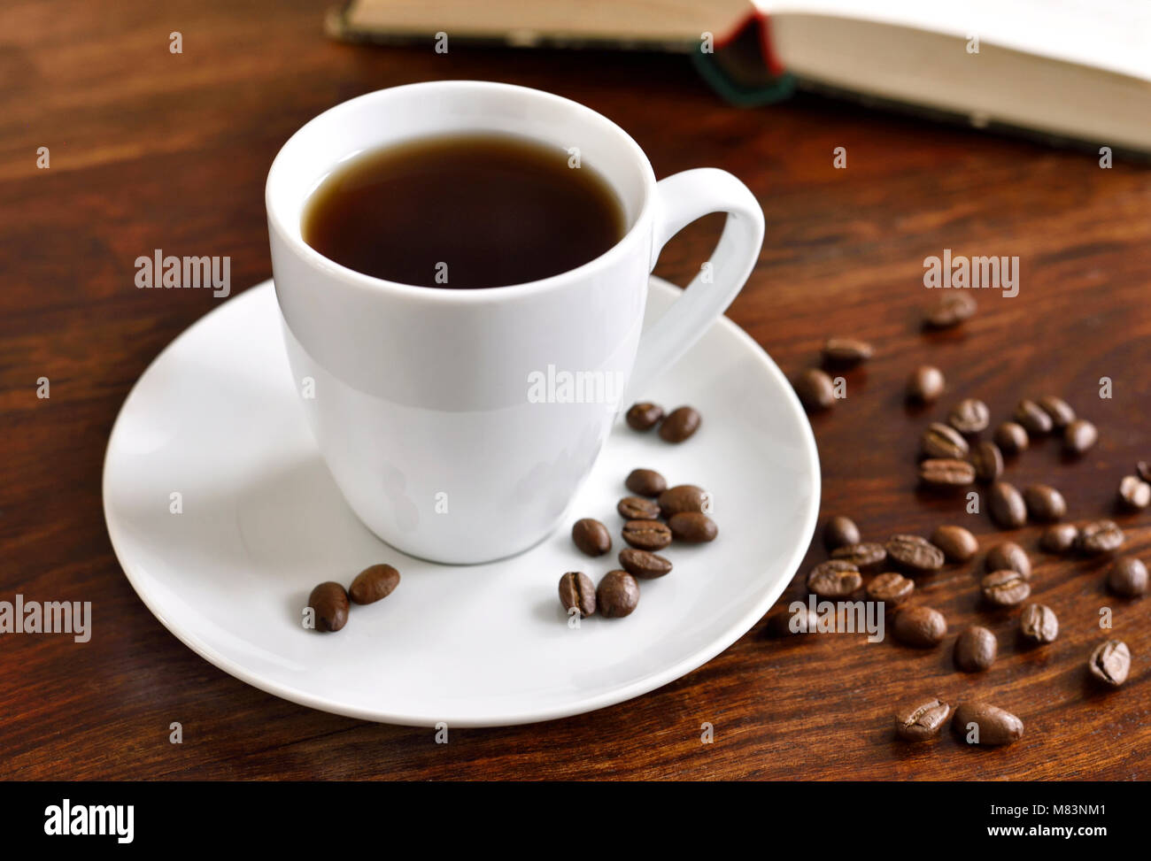 Frühstück Szene mit Kaffeetasse, offenes Buch und Kaffeebohnen auf einem Holztisch. Morgen Szene mit heißem Kaffee. Stockfoto