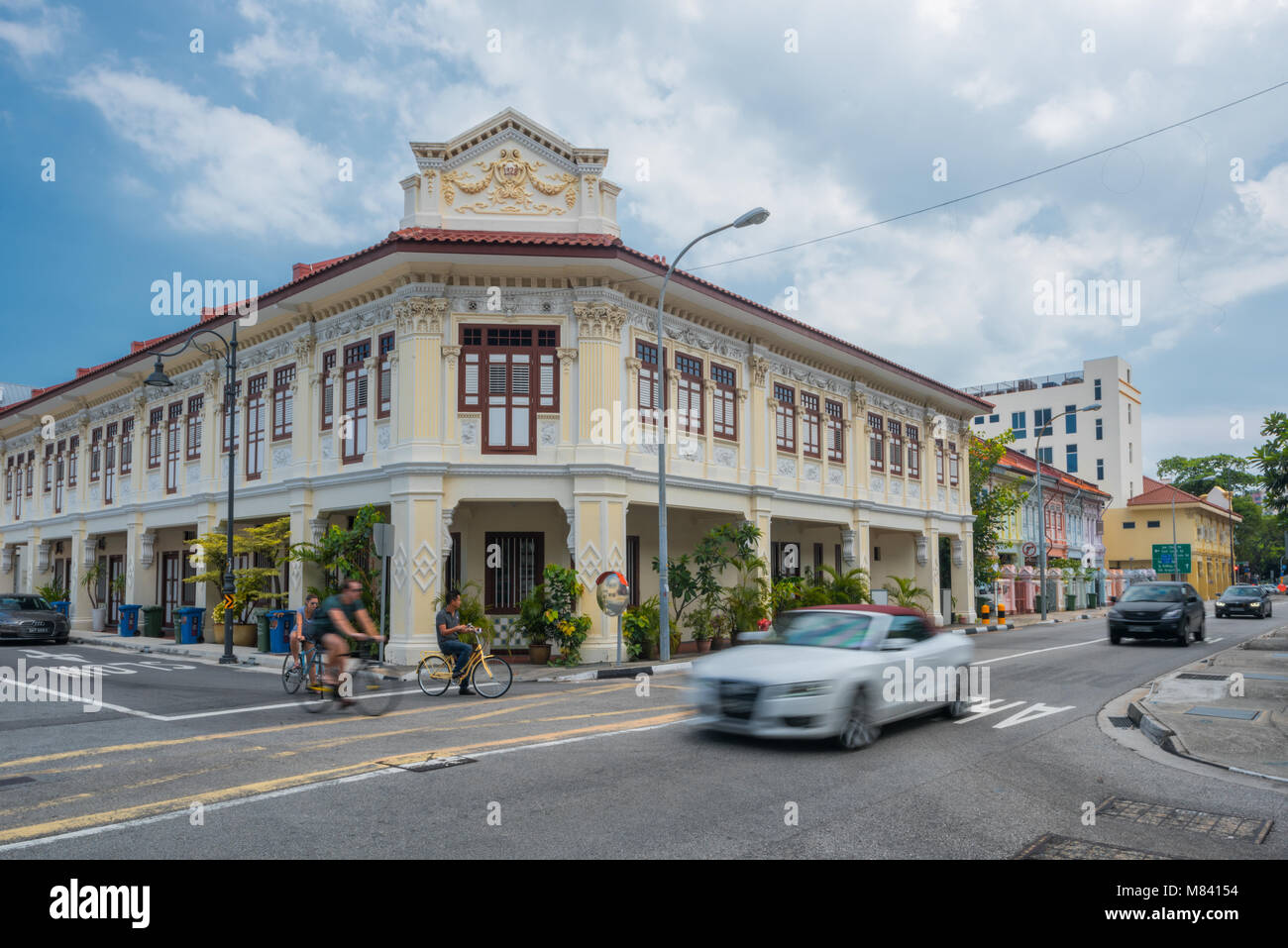 Der Kiosk an der Ecke Haus entlang Joo Chiat Road. Ein fahrendes Auto und Radfahrer sind in den Vordergrund. Stockfoto