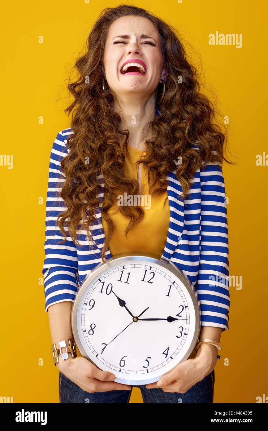 Traurig, elegante Frau mit langen Welligen brünette Haare auf gelben Hintergrund mit Uhr isoliert Stockfoto