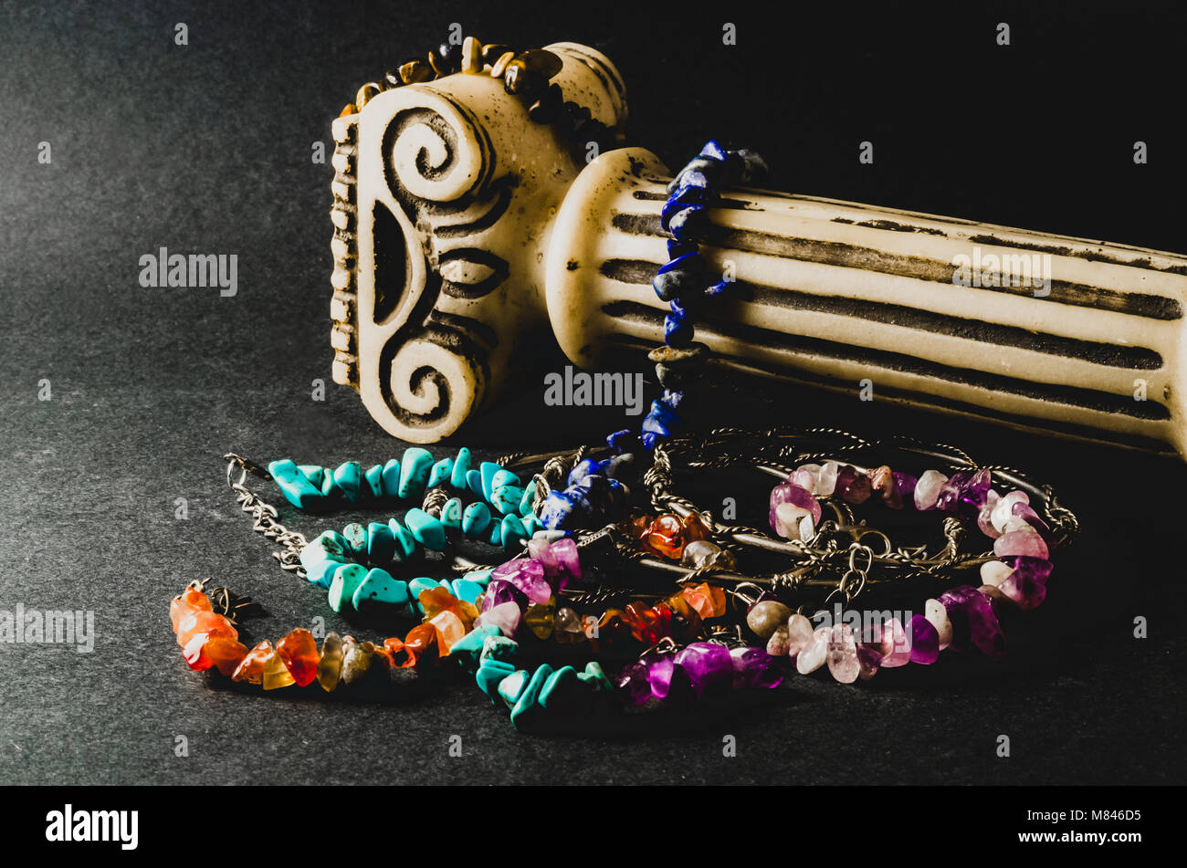 Bunte Armbänder von Natursteinen und antiken Säule auf grauem Hintergrund Stockfoto