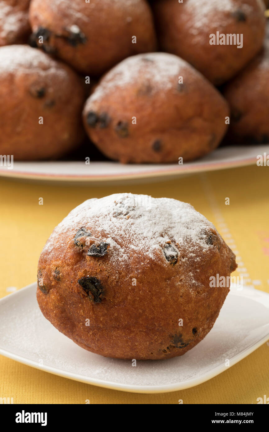 Single oliebol mit Zucker bedeckt, traditionelle niederländische Gebäck für Silvester und ein Haufen im Hintergrund Stockfoto