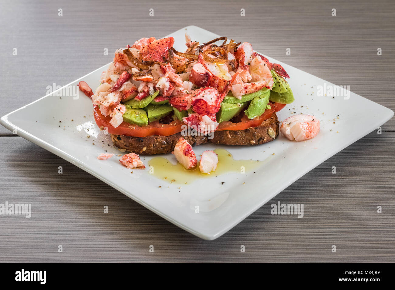 Ein weißer Teller mit ein getoastetes Sandwich mit Tomate, Avocado, übrig gebliebene Karabinerverschluss Fleisch, und knusprig gebratene Schalotten. Stockfoto