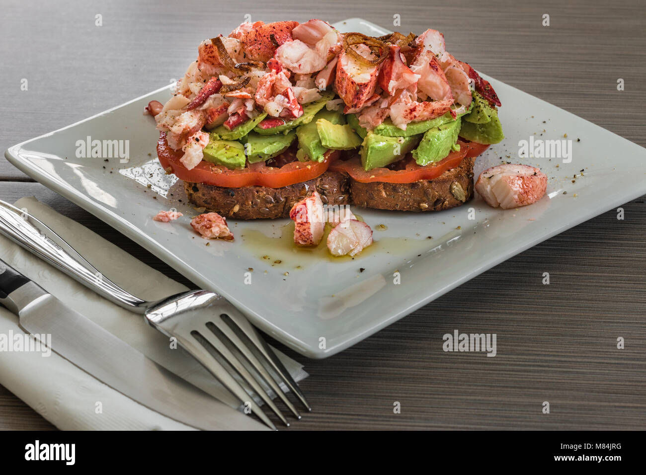 Ein weißer Teller mit ein getoastetes Sandwich mit Tomate, Avocado, übrig gebliebene Karabinerverschluss Fleisch, und knusprig gebratene Schalotten. Stockfoto