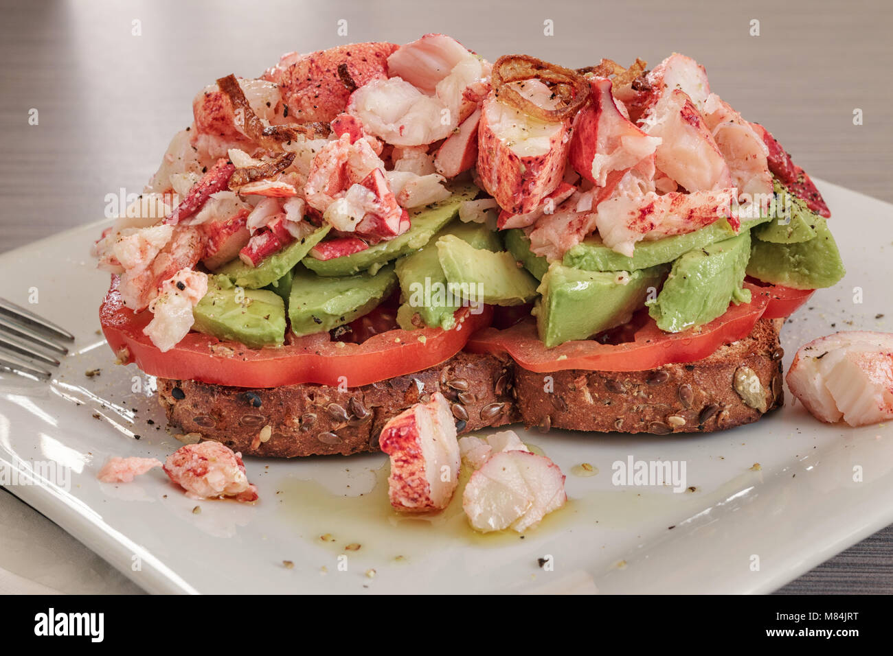 Ein weißer Teller mit ein getoastetes Sandwich mit Tomate, Avocado, übrig gebliebene Karabinerverschluss Fleisch, und knusprig gebratene Schalotten. Stockfoto