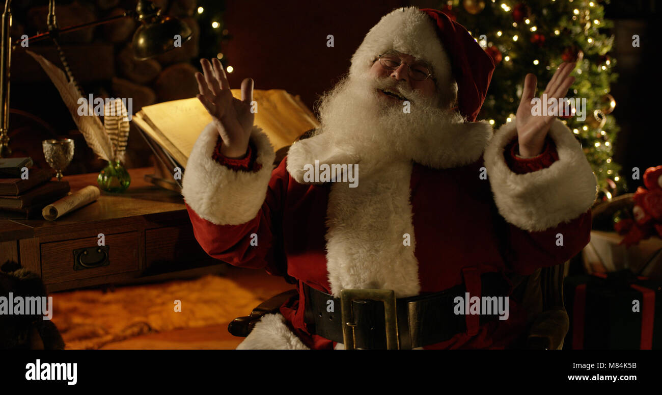 Mittellange Aufnahme des Santa Claus in voller Weihnachten Regalia, einschließlich Kappe, hebe die Arme und jolly Lachen. Stockfoto