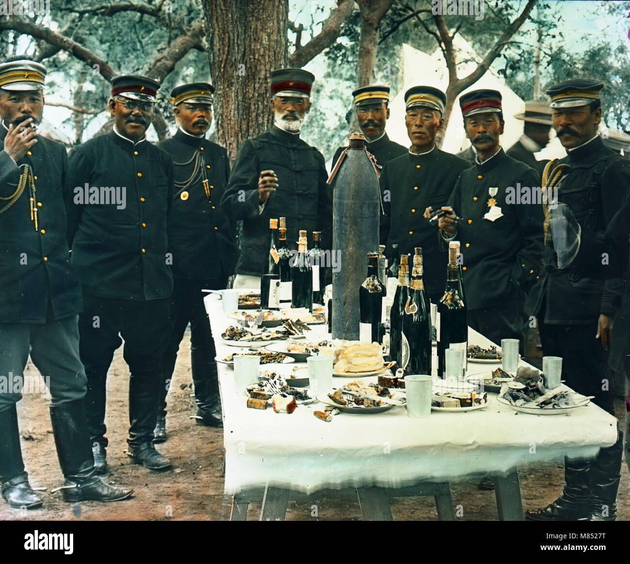 Koloriertes Foto des japanischen Generals Graf Nogi Maresuke (1849 - 1912) (Mitte) und Offiziere, die während einer Siegesfeier während des Russisch-Japanischen Krieges um einen Tisch standen, Port Arthur, China, 1905. Das eingereichte ist mit Flaschen Teller mit Lebensmitteln gefüllt, sowie eine Mörsergranate. (Foto von Burton Holmes) Stockfoto