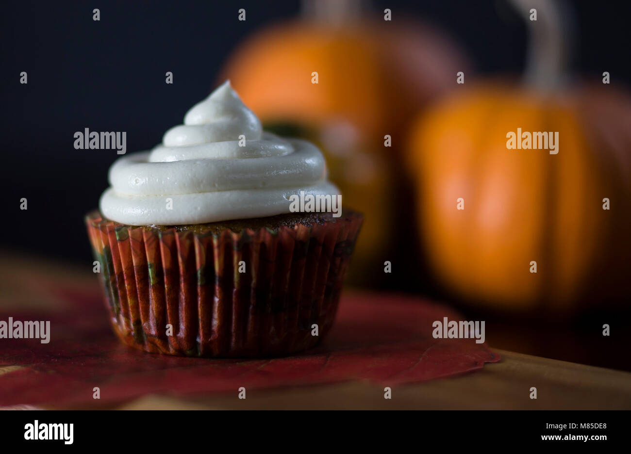 Köstliche Pumpkin Spice Cupcakes mit Cream Cheese Frosting mit Kürbissen im Hintergrund Stockfoto