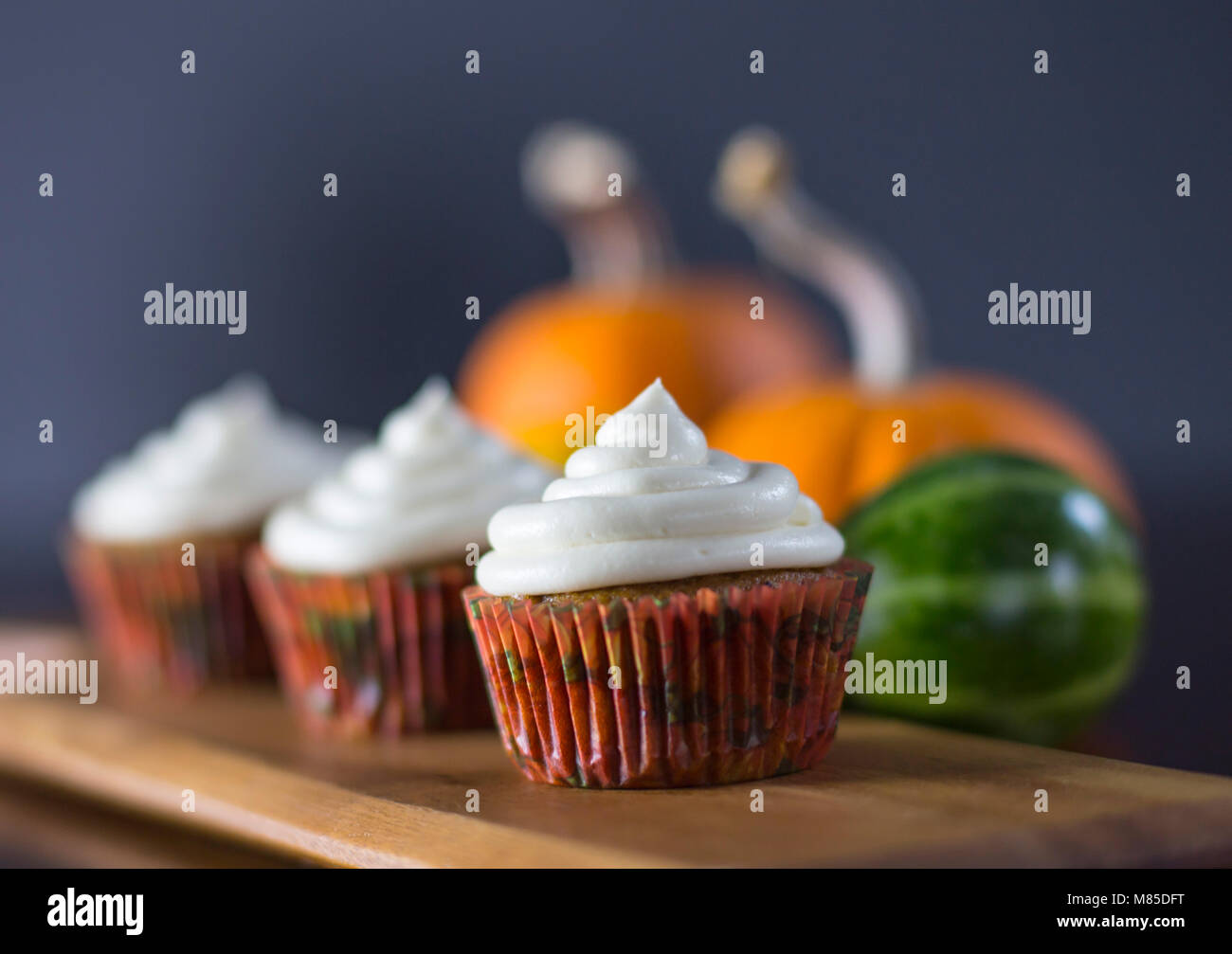 Köstliche Pumpkin Spice Cupcakes mit Cream Cheese Frosting mit Kürbissen im Hintergrund Stockfoto
