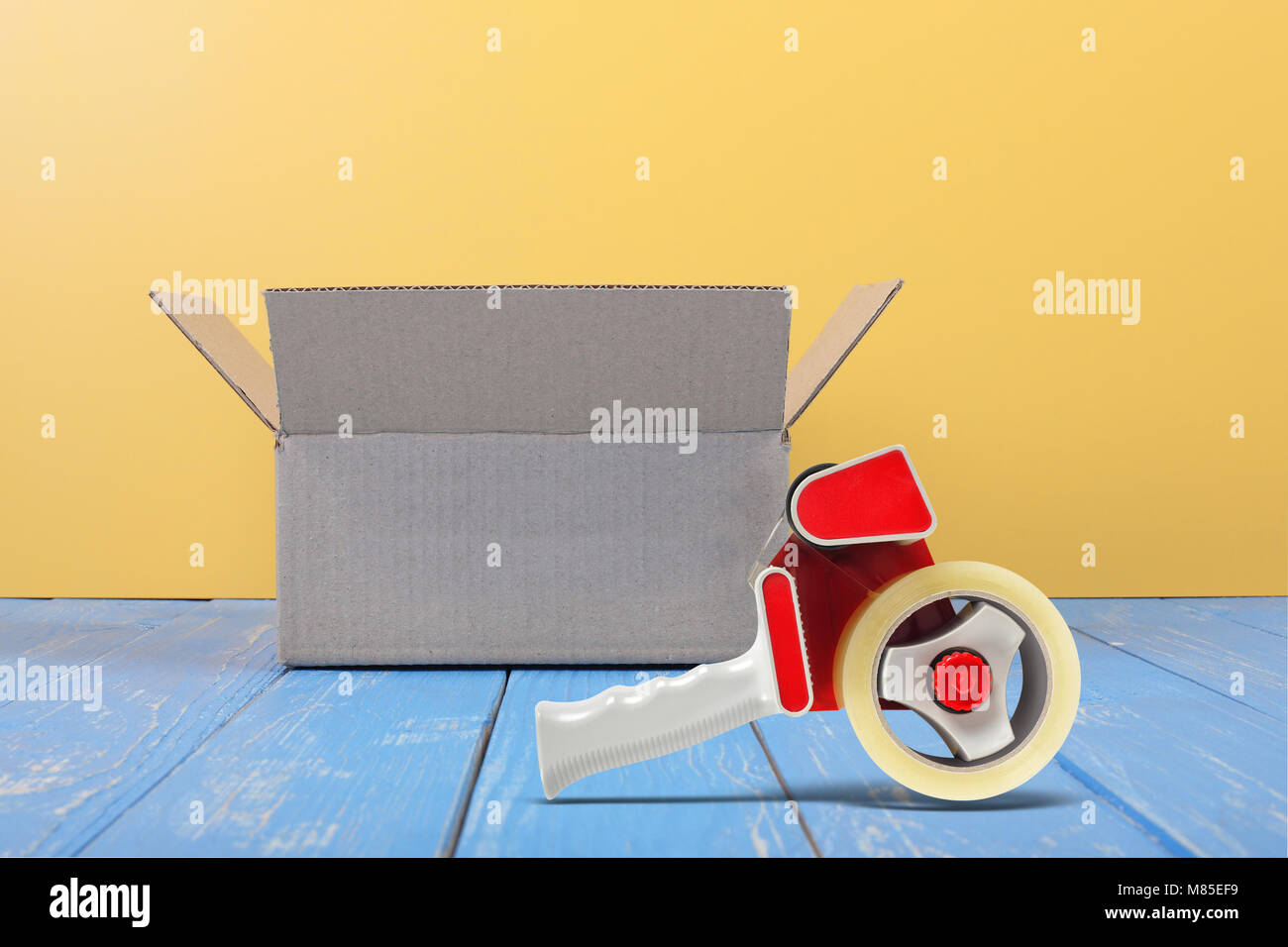 Porto und Verpackung service-Paket öffnen und Tape dispenser Vorderansicht auf blauem Holz und gelbe Wand Hintergrund. Stockfoto