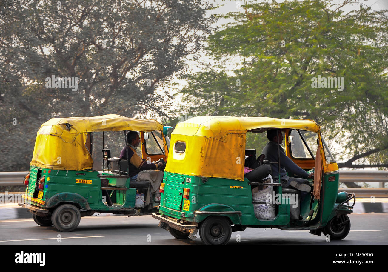Tuk Tuk's auf einer belebten Straße in Delhi, Indien. Grün und gelb gefärbte Auto-rikschas an Geschwindigkeit reisen mit Bäumen im Hintergrund Stockfoto