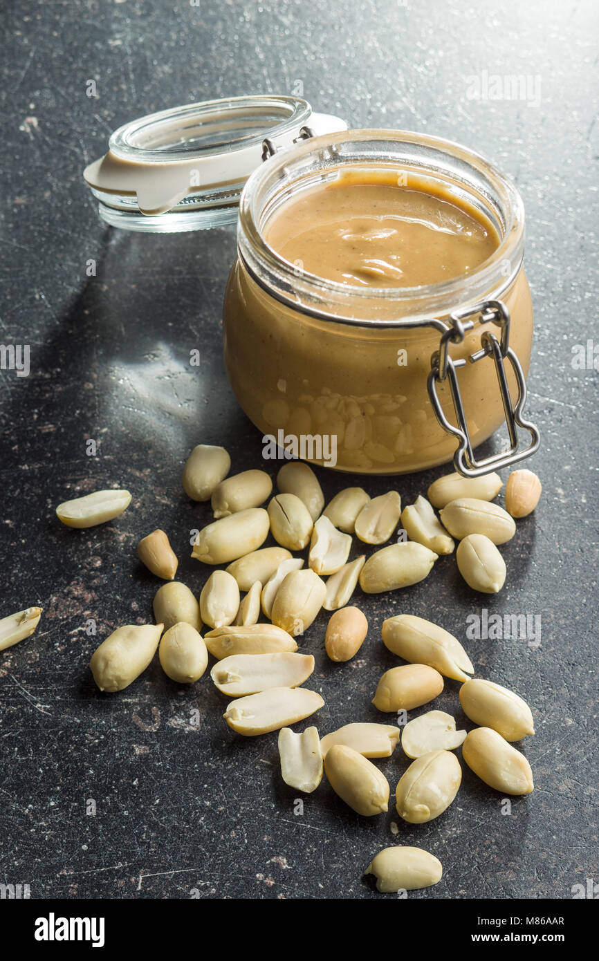 Erdnussbutter im Glas und Erdnüsse auf alten Küchentisch. Stockfoto