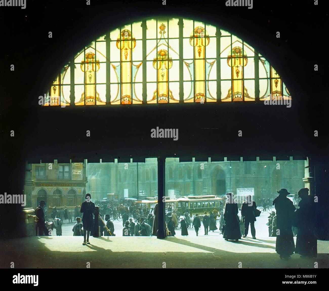 Kolorierte Ansicht des Eingangs zum Bahnhof Flinders Street, vom Innenraum aus gesehen, mit Blick auf die Kreuzung der Flinders und Swanston Street, Melbourne, Australien, 1917. Ein Jugendstil-Torbogen aus Buntglas erhellt das dunkle Interieur. Fotografie von Burton Holmes. Stockfoto