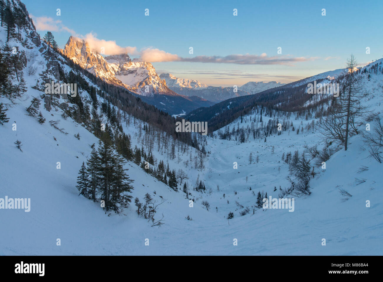Sonnenuntergang Blick auf das verschneite Tal in Richtung der Pale di San Martino, mit Skipisten und Hütte unter, bunte Wolken trieb auf die Gipfel Stockfoto