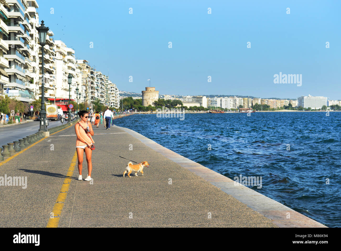 Eine Griechin, die auf der Uferpromenade mit dem Weißen Turm von Thessaloniki im Hintergrund läuft. Stockfoto