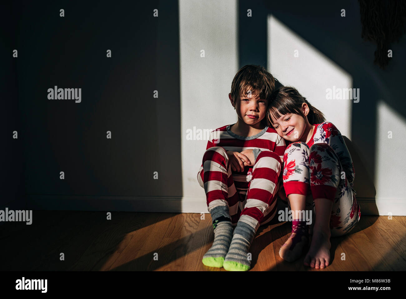 Jungen und Mädchen in Ihren Schlafanzug auf dem Boden sitzend gebadet im Sonnenlicht Stockfoto