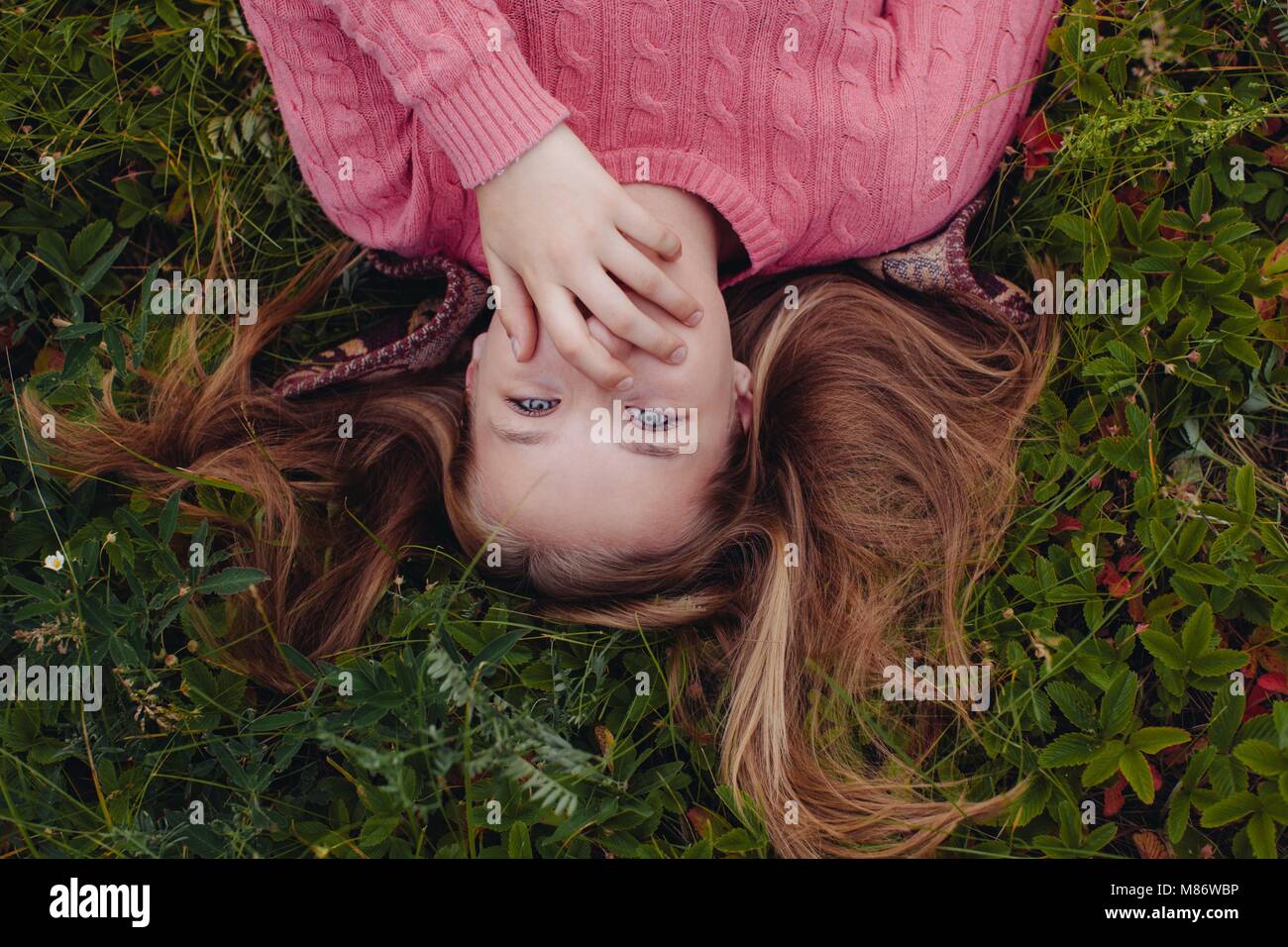 Mädchen liegt auf Gras mit der Hand über den Mund Stockfoto