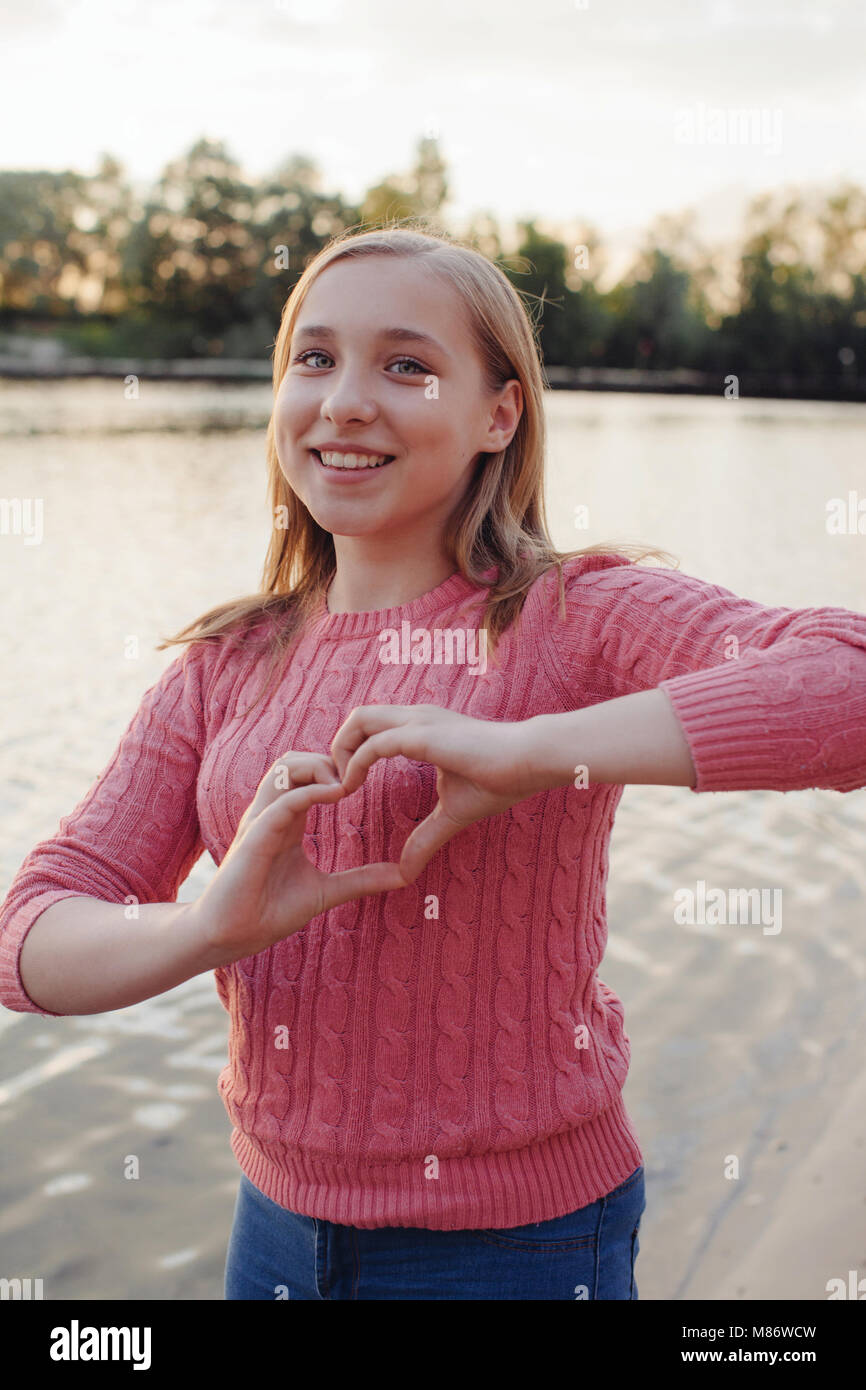 Lächelnde Mädchen durch einen Fluss, die Form eines Herzens mit ihren Händen stehend Stockfoto