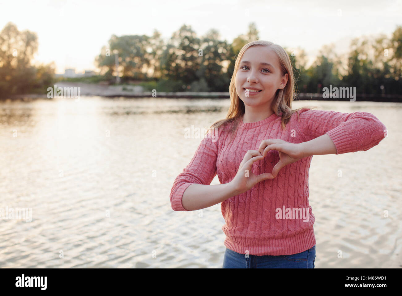 Lächelnde Mädchen durch einen Fluss, die Form eines Herzens mit ihren Händen stehend Stockfoto