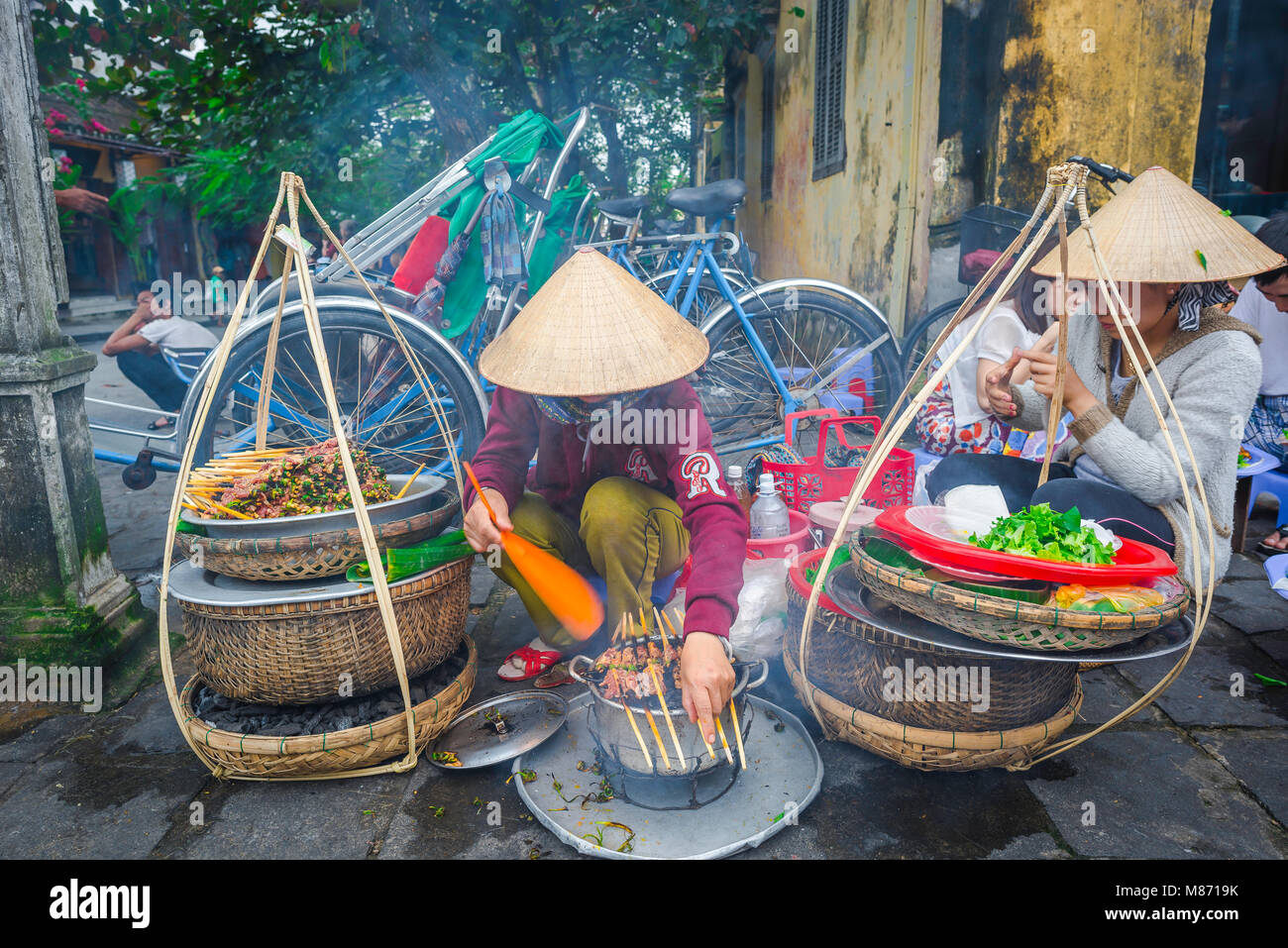 Street Food Vietnam, Blick auf zwei vietnamesische Frauen, die Schweinekebabs grillen in einer Straße in der Nähe des Ufers in Hoi an, Zentralvietnam. Stockfoto