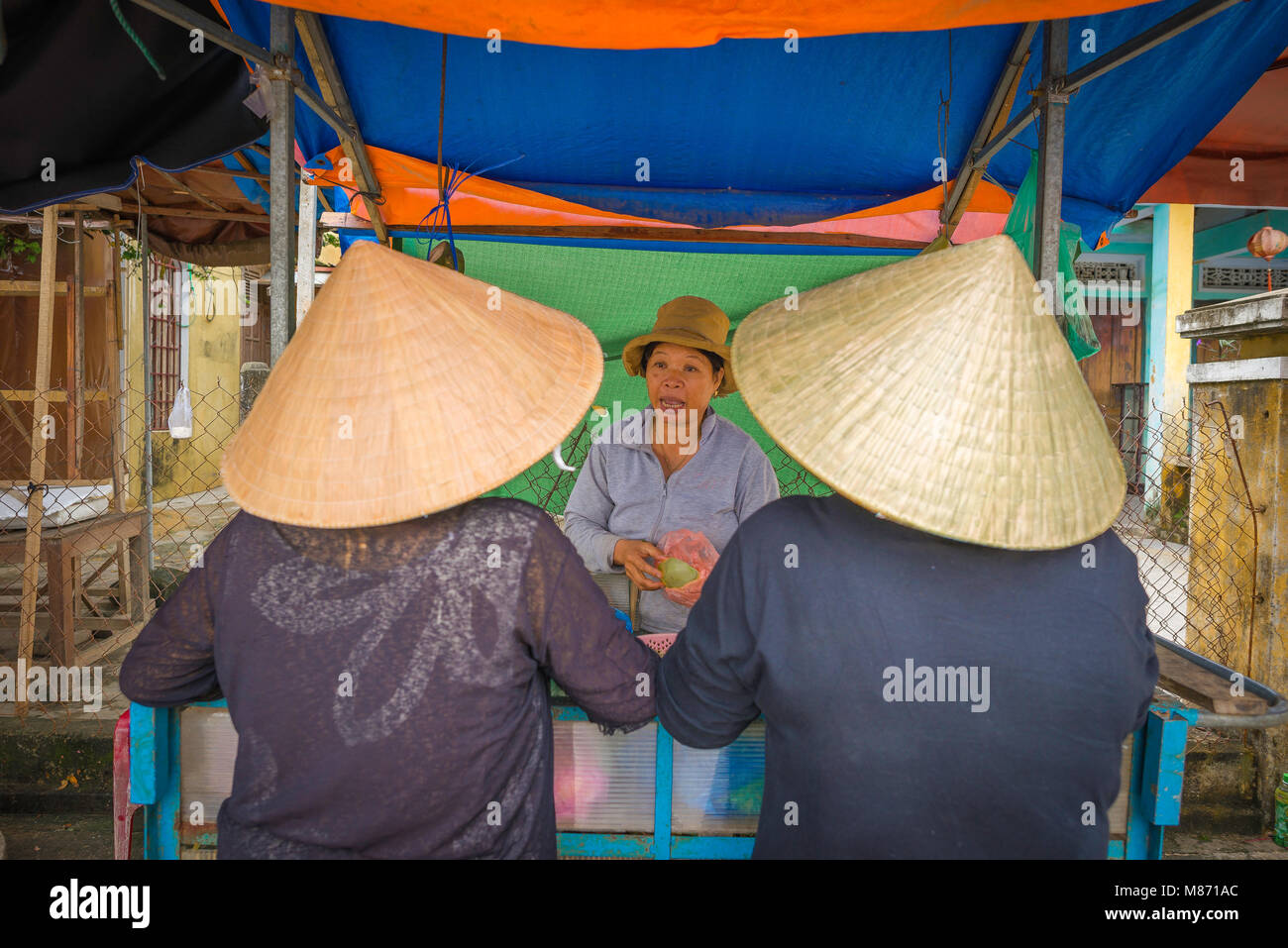 Frauen shopping Vietnam, zwei Vietnamesische Frauen mit konischen Hüten Frucht von einem flußufer Anbieter in Hoi An, Vietnam kaufen. Stockfoto