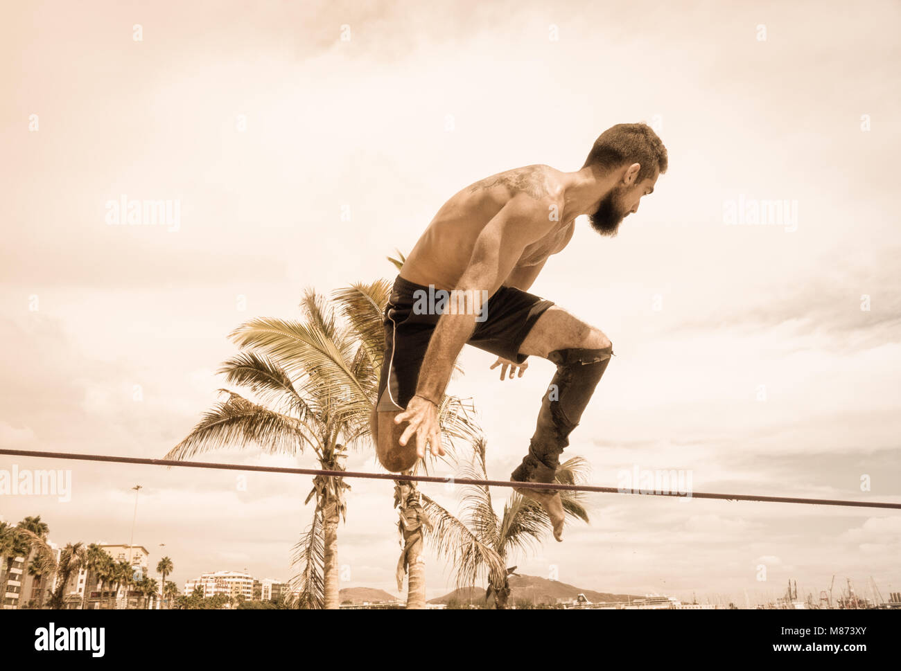 Mann, Saltos und Gymnastik demontiert auf slackline zwischen Palmen am Strand in Spanien gebunden Stockfoto