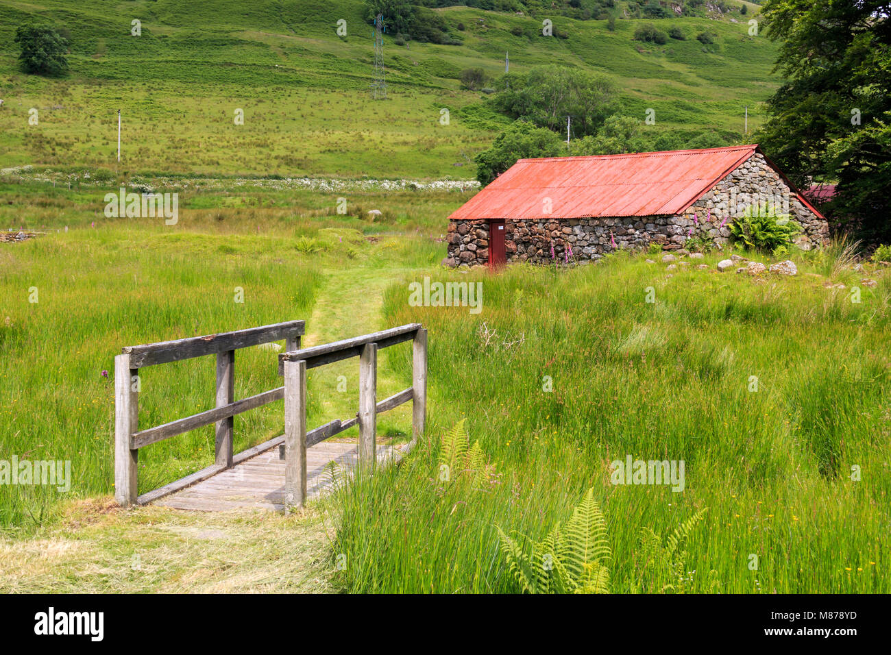 Kleinen hölzernen Brücke über einem Grasbewachsenen graben mit einem alten Bauernhaus in der Ferne Stockfoto